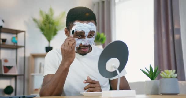 Kosmetyczny zabieg maski twarzy, w którym atrakcyjna, opiekuńcza, pozytywna, afrykańska amerykanka nakłada na twarz białą maskę pędzlem — Wideo stockowe