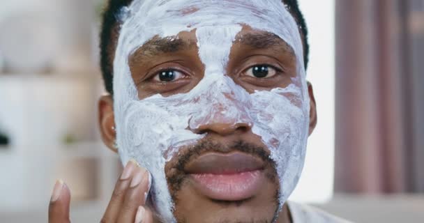 Gros plan de belle jeune afro-américaine souriante qui pose dans la caméra tout en appliquant un masque facial — Video