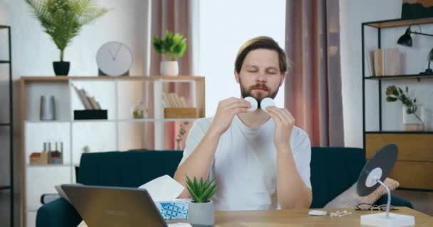Портрет привлекательного веселого расслабленного молодого бородатого парня, который сидит перед камерой и делает движения руками, очищая лицо хлопчатобумажными прокладками — стоковое видео