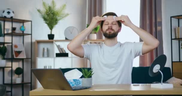 Goed uitziende kalme jonge drager zit voor de camera en veegt zijn gezicht met ronde bewegingen met behulp van katoenen pads en toont ze in de camera — Stockvideo