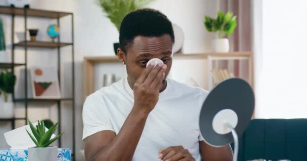 Close up de boa aparência calma moderna afro-americana que olhando para o seu reflexo em espelho redondo em casa ao limpar o rosto usando almofada de algodão — Vídeo de Stock