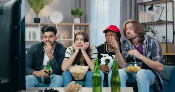 Atractivo molesto joven cuatro amigos de raza mixta viendo partido de fútbol en la televisión en casa e insatisfecho del juego de equipo favorito, vista frontal, concepto de ocio — Vídeos de Stock