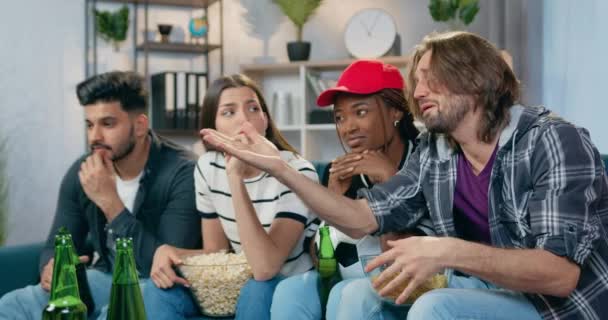 Atraktivní nešťastný mladý multiracial kamarádi nespokojeni ze hry oblíbeného týmu a mluvit o hře, když sedí před televizí doma a jíst chipsy, popcorn a pití piva — Stock video