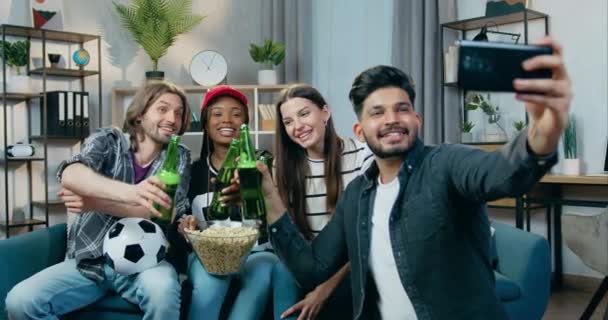 Goed uitziende glimlach gelukkig zorgeloos jonge multiraciale mensen klinkende flessen bier bij het maken van selfie tijdens home party — Stockvideo