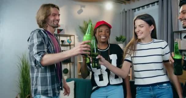 Концепція дозвілля, де добре виглядають усміхнені щасливі молоді різноманітні друзі танцюють в кімнаті під час домашньої вечірки і кмітливі пляшки з пивом — стокове відео