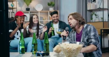 Üç güler yüzlü karışık ırk sakallı arkadaşlarını destekliyor. Ev partisi sırasında karaoke setinin önünde oturmuş mikrofonda şarkı söylüyorlar.