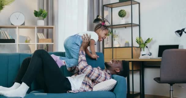 Glad afrikansk far leker med dottern på soffan — Stockvideo