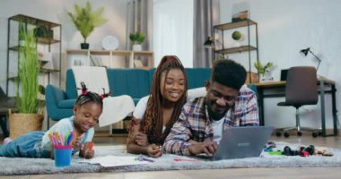 Kızı yerde çizerken ebeveynler dizüstü bilgisayar kullanıyor