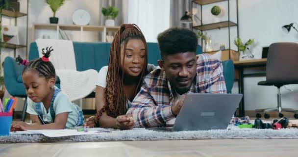 Afro parents américains en utilisant un ordinateur portable tandis que la fille dessin — Video
