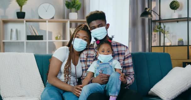 Afričtí rodiče a dcera v obličejových maskách sedí na gauči — Stock video