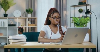 Kız tek başına oynarken, Afrikalı kadın dizüstü bilgisayarda çalışıyor.