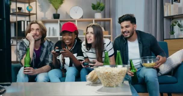 Bello sorridente emotivo misto razza quattro amici maschi e femmine divertirsi insieme mentre godendo videogiochi durante la festa di casa — Video Stock