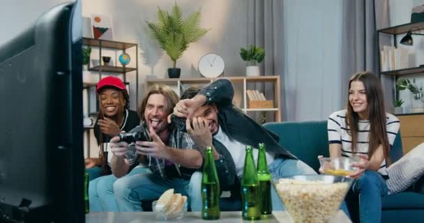 Veselý legrační emocionální smíšené závod společnost sedí před televizí a těší videohry slaví vítězství s dávat vysoké pětky a směje se — Stock video