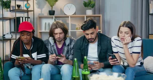 Dependence on phones problem where attractive concentrated modern young mixed race friends sitting on the couch at home and everybody use his mobile — Stock Video