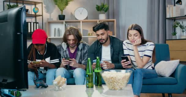 Çekici, konsantre, dört farklı modern arkadaş birinin evinde kanepede oturuyor ve uygulamaları veya videoları izlemek için akıllı telefonlar kullanıyor. — Stok video