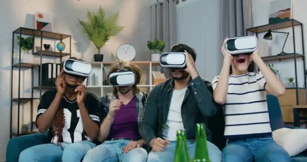 Front view of adorable smiling happy four mixed race freinds which celebrating victory in videogames using augmented reality goggles during home party — Stock Video