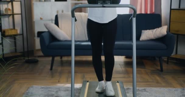 Jolie jeune femme mariée heureuse et souriante en vêtements d'entraînement marchant sur tapis roulant à la maison et lisant de bonnes nouvelles sur smartphone, concept de mode de vie sain — Video