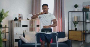 Keyifli, yorgun, modern, siyah tenli bir adam. Kardiyo egzersizleri yaparken koşu parkurunda koşuyor.