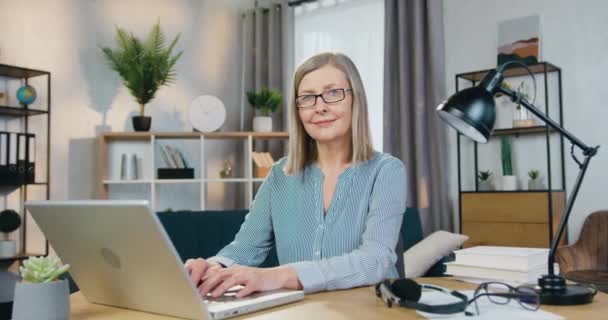 Senior woman in eyewear sitting at table with modern laptop — Stock Video