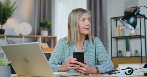 Gelukkig oud vrouw op zoek opzij terwijl het houden van smartphone — Stockvideo