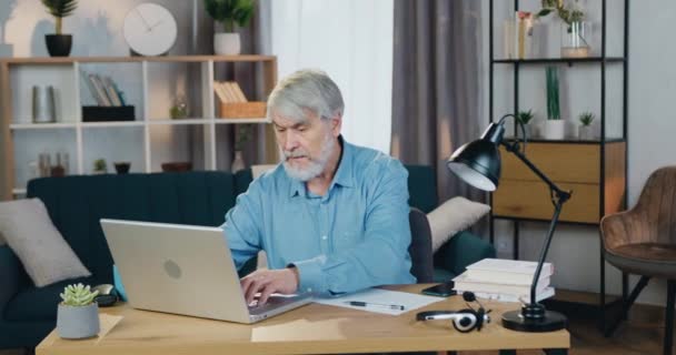 Uomo in pensione che utilizza il computer portatile per controllare le bollette a casa — Video Stock