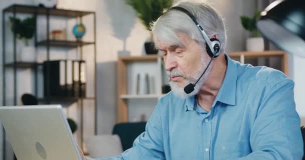 Vieil homme utilisant un ordinateur portable et un casque pour la conversation vidéo — Video