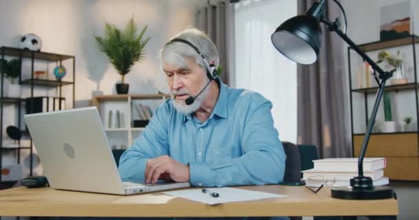 Γκρίζος άντρας με ακουστικά που έχει τηλεδιάσκεψη στο λάπτοπ — Αρχείο Βίντεο