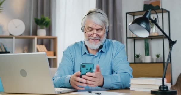 Senior man använder mobil när du sitter vid skrivbordet med bärbar dator — Stockvideo