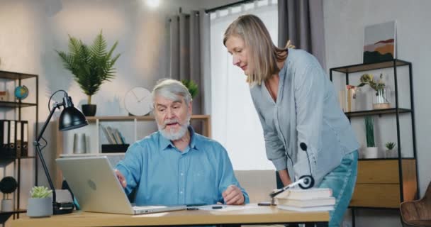 Äldre skäggiga mannen visar något för sin fru på laptop — Stockvideo