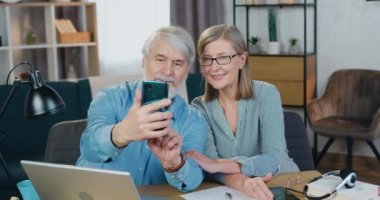 Gülümseyen olgun bir çift selfie çekmek için akıllı telefon kullanıyor.