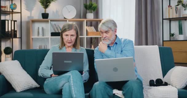 Hombre y mujer ancianos que se relajan en el sofá con computadoras portátiles en las rodillas — Vídeos de Stock