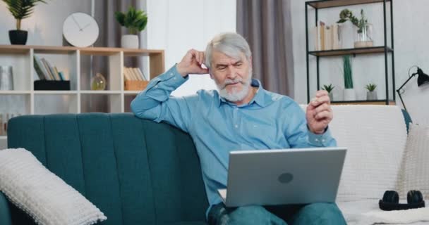 Senior man sitting on couch and having video call on laptop — Stock Video