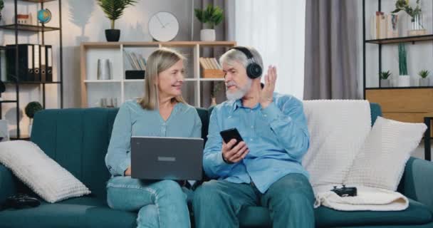 Hombre en auriculares escuchando música mientras que la mujer usando el ordenador portátil — Vídeos de Stock