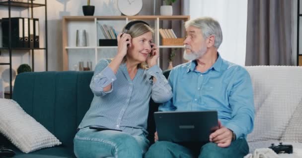 Zwei glückliche Rentner mit drahtlosem Laptop und Kopfhörer
