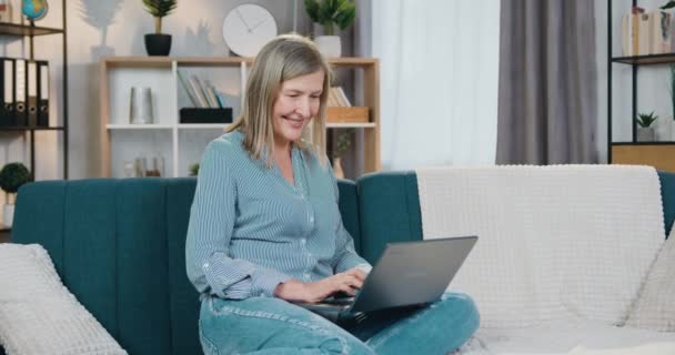 Wanita dewasa santai menggunakan laptop di sofa — Stok Video