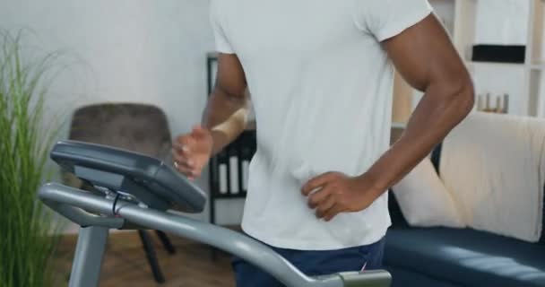 Unknown fit active african american guy holding bottle of water in one hand while running on treadmill during home workout,slow motion — Stock Video