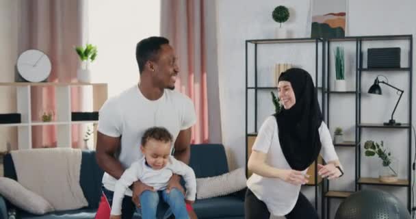 Close up of lovely happy positive active sporty multiethnic couple with small son which squating together during home training ,healthy lifestyle concept — Stock Video