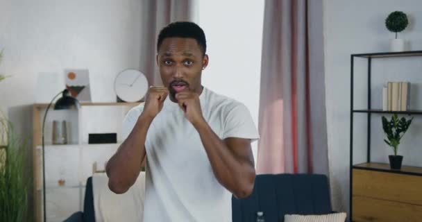 Närbild av snygg aktiv positiv ung afrikansk amerikansk man som tränar i boxning slag under hemmaträning — Stockvideo