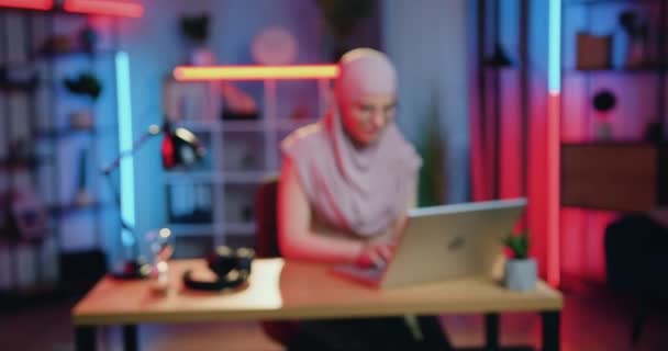 Kamera zblízka pohled na dobře vypadající šťastný úsměv kvalifikované mladé muslimské podnikatelky v hidžábu, která pracuje na svém pracovišti doma ve večerních hodinách — Stock video