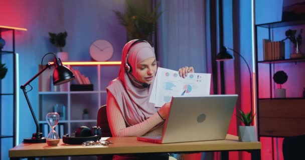 Concept de travail à distance où belle jeune femme musulmane confiante et réussie en foulard expliquant la carte lors de la vidéoconférence par ordinateur dans une pièce éclairée le soir — Video