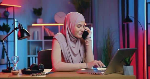 Piękna uśmiechnięta młoda, odnosząca sukcesy muzułmańska bizneswoman w nadgodzinach na głowie, pracująca w domu w nocy i rozmawiająca przez telefon komórkowy — Wideo stockowe