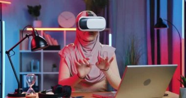 Güzel ruh hali içinde, akşamları evde özel 3D gözlüklerle sanal ekran üzerinde çalışan, tesettürlü, modern Arap bayanı kapat.