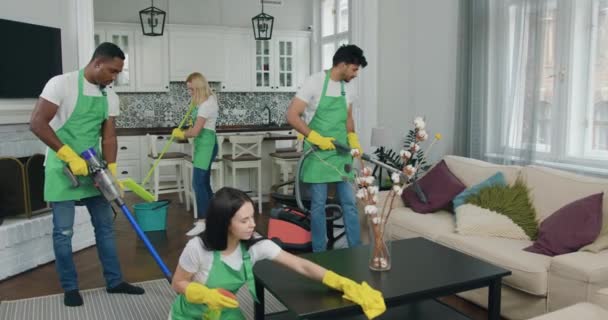 Sannolikt nöjda ansvarsfulla unga skiftande arbetstagare från städföretag städa upp moderna lägenhet med dammsugare och olika rengöringsmedel — Stockvideo