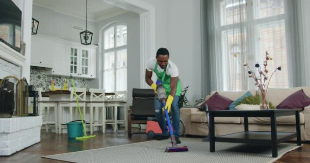 Szerethető vidám szórakoztató 30 éves fekete bőrű dolgozó takarítás szolgáltatás szórakozás, míg takarítás ügyfélház porszívó — Stock videók