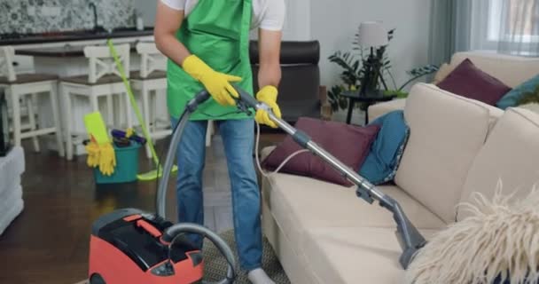 Beau confiant professionnel barbu jeune homme-travailleur de service de nettoyage à l'aide d'acariens de poussière d'aspirateur sur canapé confortable dans la cuisine-studio contemporaine — Video