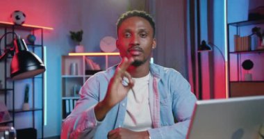 Yakışıklı, gülümseyen, 30 yaşında, siyah tenli, sıradan elbiseli bir adamın portresi. Akşamları kameranın önünde oturuyor ve güzel bir sembolle ellerini gösteriyor.