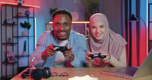 Menselijke emoties concept waar goed uitziende gelukkig glimlachen opgewonden multiraciale man en vrouw genieten van videospelletjes en vieren overwinning met high five in de avond — Stockvideo