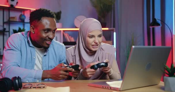 Концепция человеческих эмоций, где привлекательные современные позитивные молодые смешанные расы женщины и мужчины друзья веселятся вместе во время игр на ноутбуке, женщина выигрывает и высмеивает партнера-неудачника — стоковое видео
