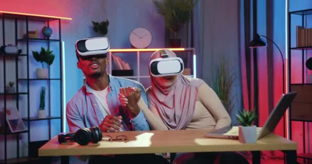 Close-up van aantrekkelijke tevreden opgewonden gemengde ras paar dat geniet van futuristische visie met behulp van augmented reality bril besteden gezamenlijke vrije tijd thuis in de avond — Stockvideo