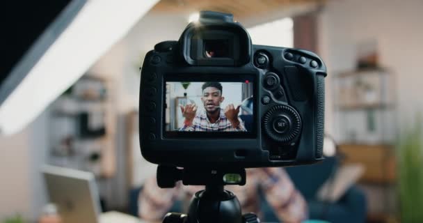 Vue à travers la caméra objectif où beau sourire confiant jeune blogueur afro-américain enregistrement vidéo pour le public Internet — Video